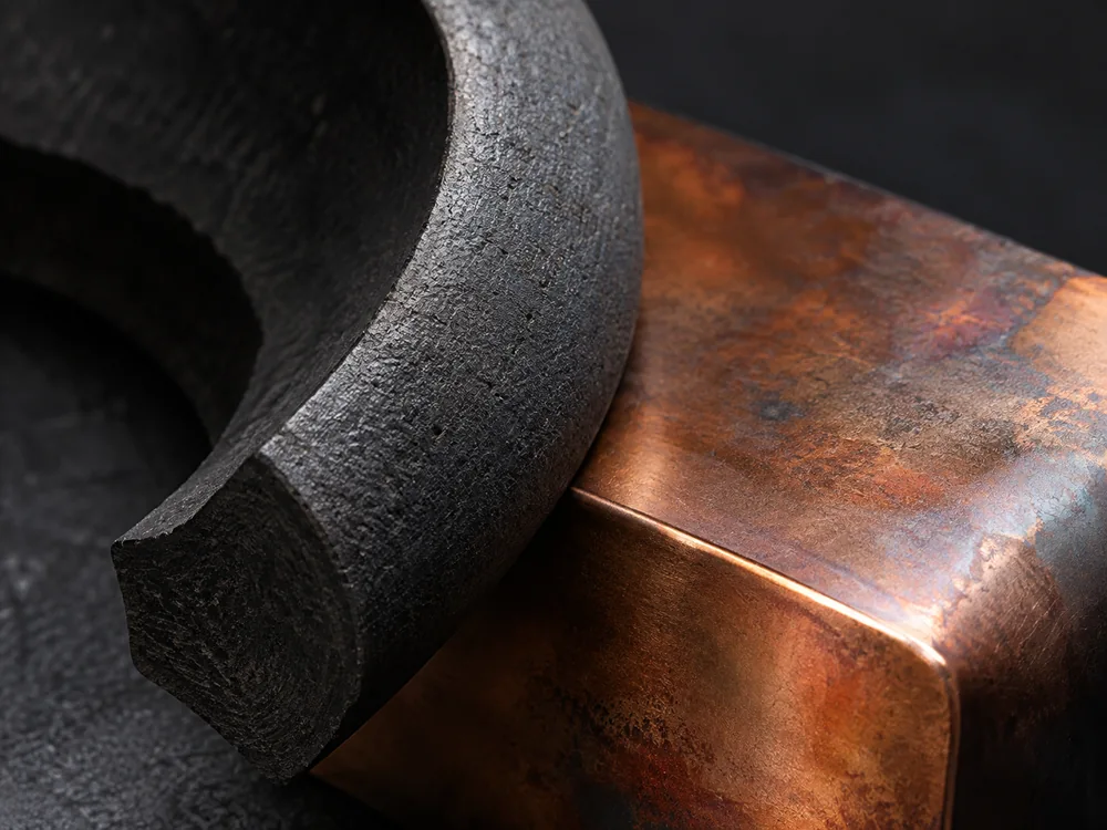Conceptual close-up of dark ceramic and copper surfaces under raking light.